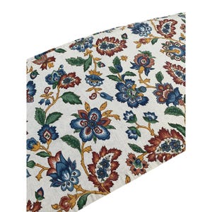 May include: A textile fabric featuring a repeating floral pattern on an off-white background. The design includes stylized blue, rust-red, and yellow flowers with green leaves and winding stems, creating a dense botanical print across the surface.