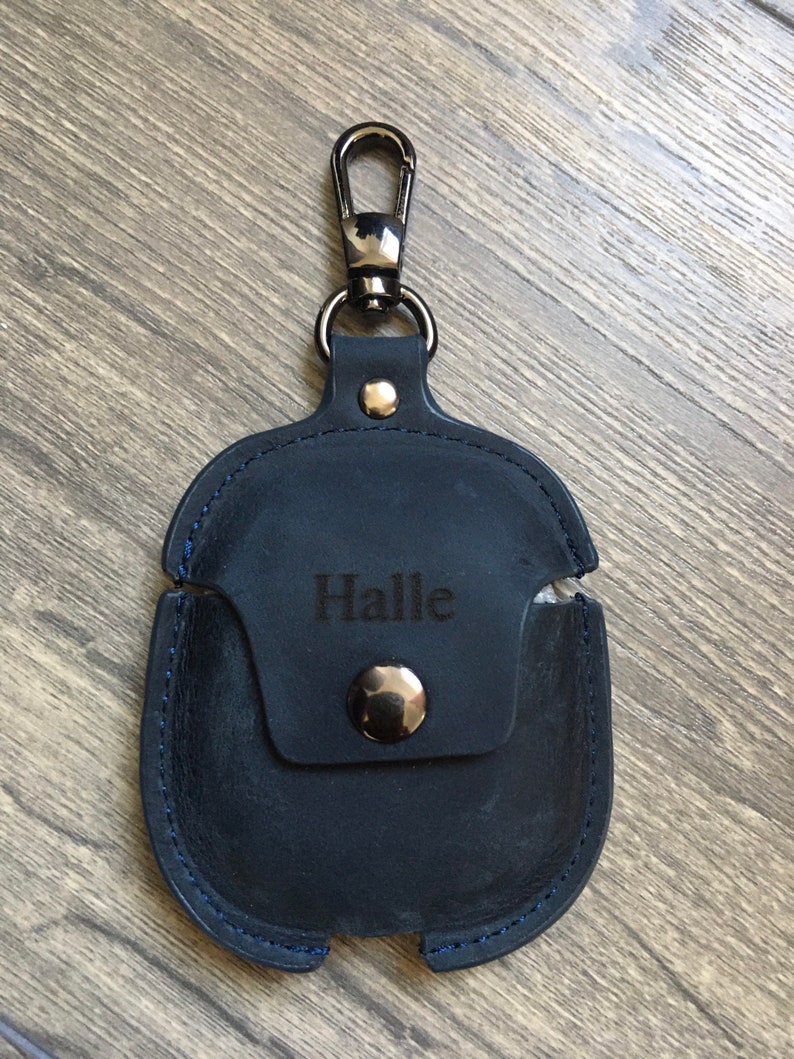 May include: A dark blue leather case with a silver clasp and a metal button. The case has a blue stitching detail and the name "Halle" is engraved on the front.
