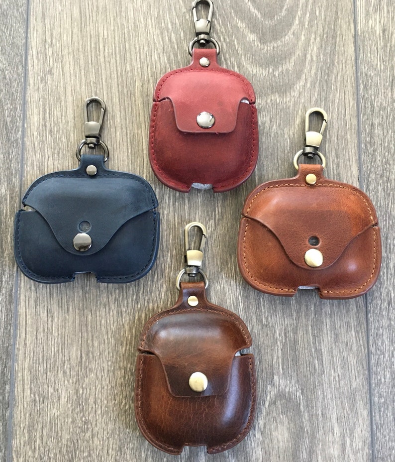 May include: Four leather Airpod cases with keychains. The cases are in red, brown, blue, and dark brown.