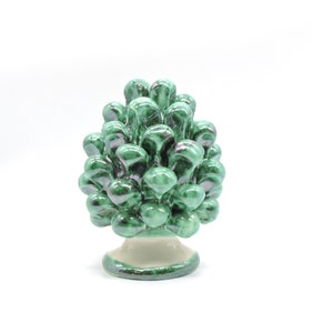 Könnte beinhalten: Ein grüner Keramik-Pinienzapfen-Anhänger mit weißem Sockel. Der Pinienzapfen ist mit einer glänzenden Oberfläche verziert und hat eine realistische Form.