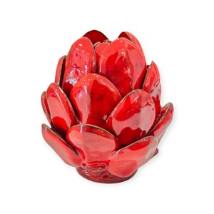 Könnte beinhalten: Eine glänzende, leuchtend rote Keramikskulptur in Form einer Artischocke. Das Objekt besteht aus mehreren überlappenden, abgerundeten, blütenblattartigen Schichten, die von einem zentralen Punkt nach außen strahlen und eine dichte, texturierte Form bilden.