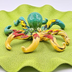 May include: A colorful ceramic octopus with yellow, red, and blue tentacles. The octopus is sitting on a green woven mat.