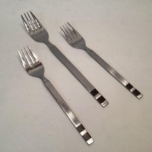 May include: Three stainless steel forks with a modern design. Each fork has a long, rectangular handle with a series of dark brown and silver stripes near the end. The tines are thin and evenly spaced.