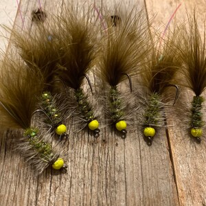 May include: Six brown and green fly fishing lures with yellow beads. The lures have long, feathery tails.