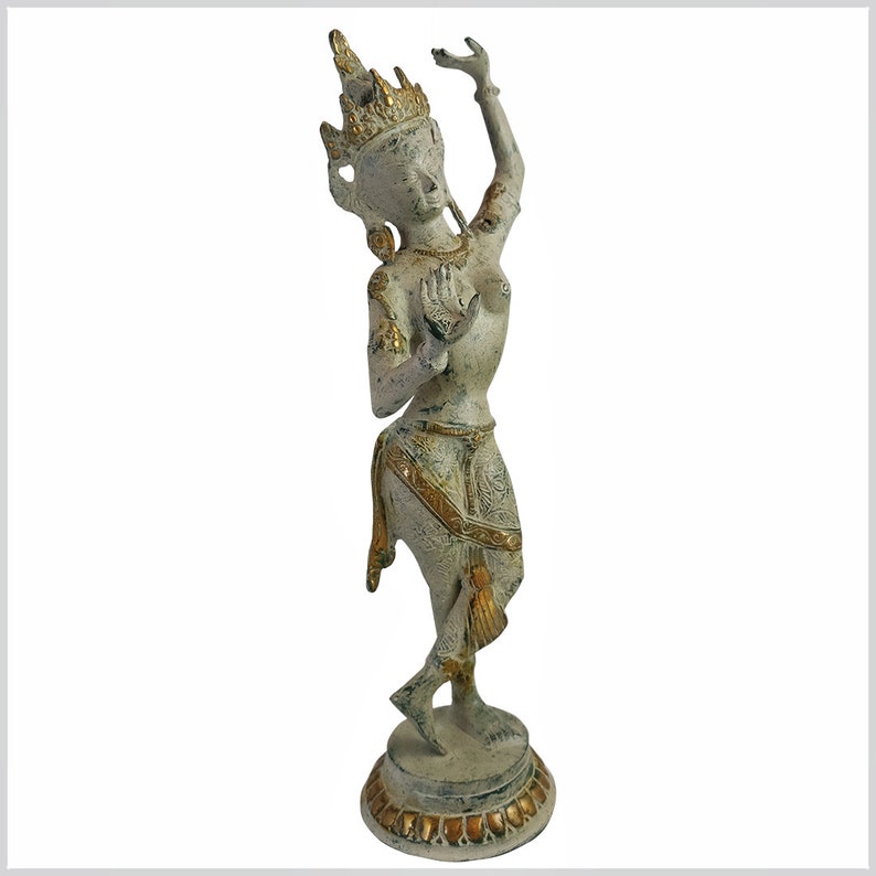 May include: A white and gold painted bronze statue of a female dancer with a crown and elaborate jewelry. The statue is standing on a round base with a decorative design.
