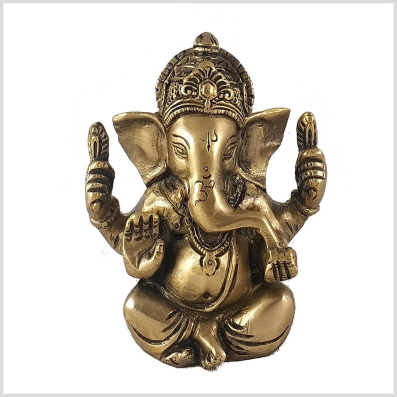 K&ouml;nnte beinhalten: Eine goldfarbene Messingstatue der hinduistischen Gottheit Ganesha. Die Statue zeigt Ganesha sitzend mit erhobenem R&uuml;ssel und seinen H&auml;nden in einer Mudra. Er tr&auml;gt eine Krone und Schmuck.