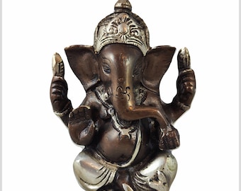 May include: A small, bronze-colored statue of the Hindu deity Ganesha. The statue is sitting with its legs crossed and its trunk raised. The statue is decorated with silver accents, including a crown on its head.