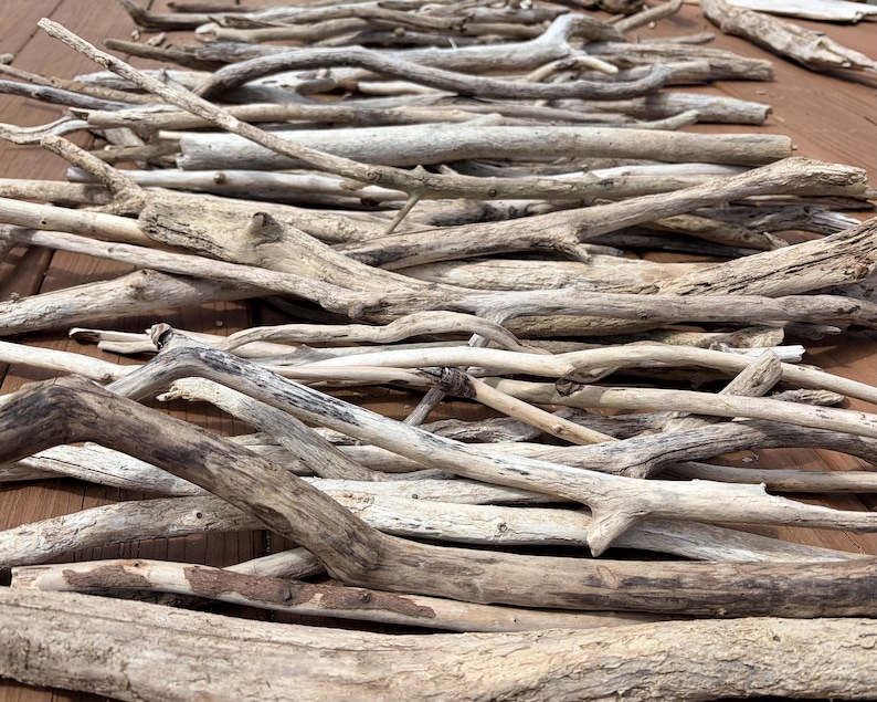 May include: A collection of weathered driftwood pieces in various sizes and shapes. The wood ranges in color from light beige to dark brown, with visible grain and texture. The pieces are arranged on a wooden surface, suitable for crafts or decor.
