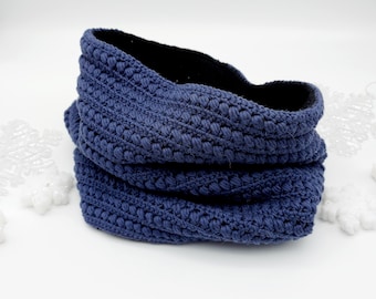May include: A blue crocheted neck warmer with a black fleece lining. The neck warmer is folded and sitting on a white surface.