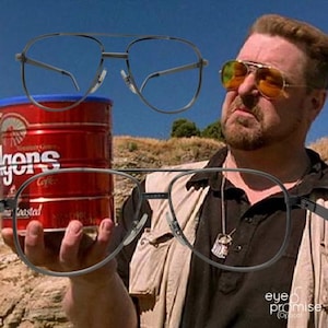 May include: Two pairs of aviator-style spectacles with dark metal frames. One pair is positioned above a red coffee tin, while the other is being worn. The glasses have a classic, timeless design.