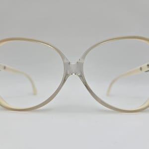 May include: A pair of large, round, cream-colored eyeglasses with clear lenses.