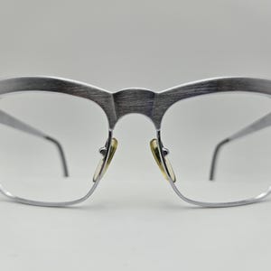 May include: Silver-toned metal eyeglasses with a brushed finish and a rectangular frame.