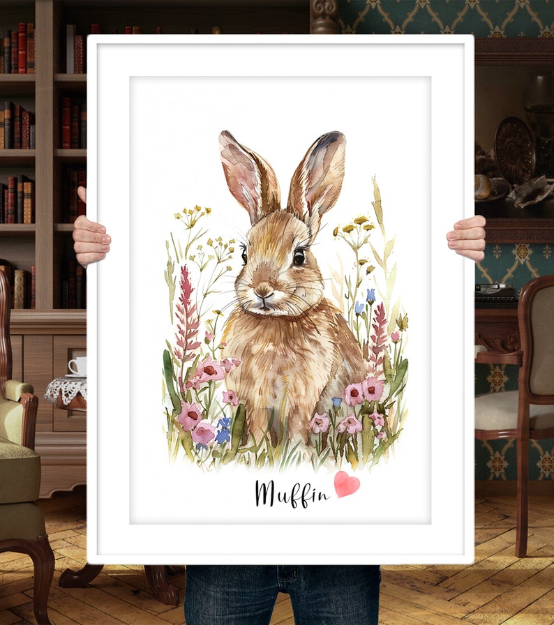 Puede incluir: Una pintura de acuarela de un conejo marr&oacute;n sentado en un campo de flores silvestres. El conejo est&aacute; mirando directamente al espectador. Las flores son rosas, azules y amarillas. El texto "Muffin" est&aacute; escrito debajo del conejo, con un coraz&oacute;n rosa al lado.