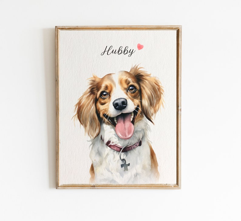 May include: Watercolor painting of a dog with brown and white fur, wearing a burgundy collar with a silver tag. The dog is smiling with its tongue sticking out. The painting is framed in a light wood frame and has the word "Hubby" written in black cursive above the dog with a small red heart.