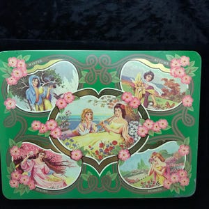May include: A rectangular green metal tin featuring illustrations of the four seasons. Each scene depicts a woman in a different setting, with the words "Winter", "Autumn", "Spring", and "Summer" displayed. Pink floral accents frame each scene.
