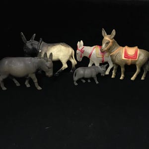 May include: A collection of six toy donkeys in various colors, including gray, black, and tan. Some donkeys have saddles and decorative elements. The donkeys are arranged on a black surface.