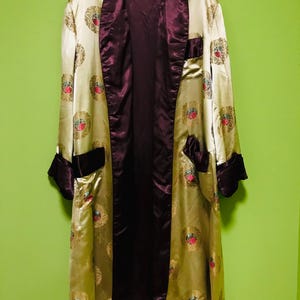 May include: A long, satin robe in shades of gold and burgundy, adorned with a repeating circular pattern featuring red and gold floral designs. The robe has a shawl collar, pockets, and cuffs in a darker burgundy color.