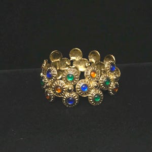 May include: A gold-toned metal link bracelet featuring a series of circular, textured medallions. Each medallion is set with a small, smooth, translucent cabochon stone in vibrant shades of blue, green, and orange, arranged in a repeating pattern.