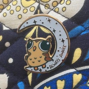 May include: Gold-tone pin featuring a cartoon owl with big eyes and the text "Always Awake" on a crescent moon.