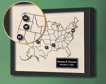 May include: A black and white map of the United States with black circles on it. The circles have text inside them, such as "Our Home", "First Apt", "Game Days", "Family", and "Next Trip". The map is framed in black and has a black plaque at the bottom that says "Brianna & Victoria November 27, 2022".