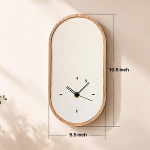 May include: An oval wall clock with a light wood frame and a white face. The clock features black hands and simple black dash markers for the hours. Dimensions are clearly marked as 10.5 inches in height and 5.5 inches in width on the image.