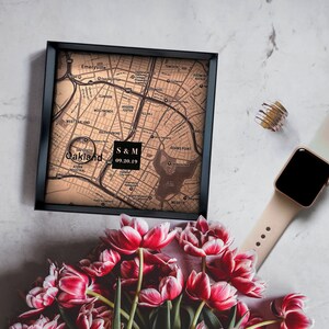 Puede incluir: Un mapa de Oakland, California, enmarcado en negro, con el texto "S & M 09.20.19" en un cuadro blanco. El mapa est&aacute; sobre una superficie blanca con un ramo de tulipanes rosas y un Apple Watch de oro rosa.