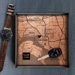 Puede incluir: Un mapa de madera de San Diego con un coraz&oacute;n negro marcando la ciudad. El mapa est&aacute; en un marco negro e incluye el texto "S & H 1.9.2002". Una llave de coche negra est&aacute; en el mapa.