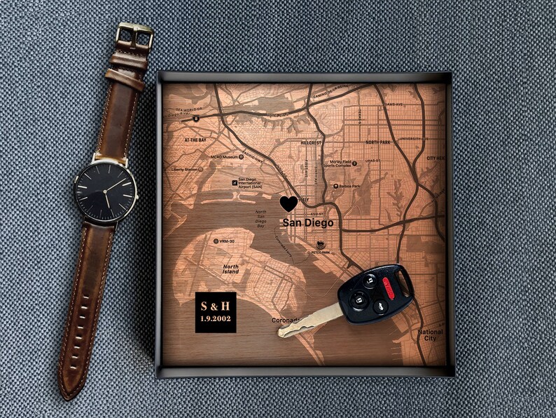 Puede incluir: Un mapa de madera de San Diego con un coraz&oacute;n negro marcando la ciudad. El mapa est&aacute; en un marco negro e incluye el texto "S & H 1.9.2002". Una llave de coche negra est&aacute; en el mapa.