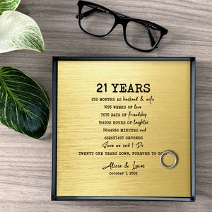 May include: A gold-colored metal plaque with black text commemorating 21 years of marriage. The plaque reads "21 Years", "252 Months as husband & wife", "1095 Weeks of love", "7670 Days of friendship", "184082 Hours of laughter", "11044958 Minutes and 662697497 Seconds", "Since we said I Do", "Twenty One Years Down, Forever to Go", "Alicia & Lucas", "October 1, 2002".