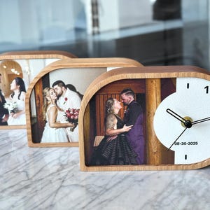 May include: Three semi-circular wooden desk clocks featuring custom photo prints of couples. The front-most clock displays a photo of a couple, a white circular clock face with black hands, and the printed date 08-30-2025 on the white surface.