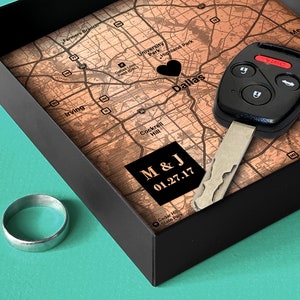 May include: A black box with a wooden map inside. The map is of Dallas, Texas and has a heart marking the center of the city. A car key is on top of the map. The box also contains a silver ring. The map has the text "M & J 01.27.17" on it.
