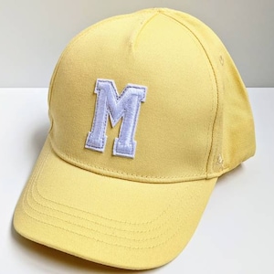 Può includere: Un berretto da baseball giallo con una lettera "M" in feltro bianco sul davanti.