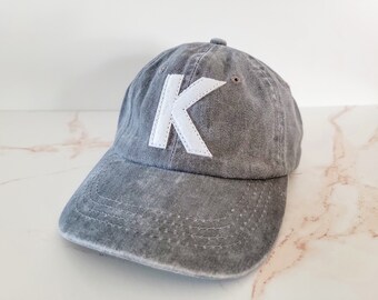 May include: A grey denim baseball cap with a white felt letter K on the front.