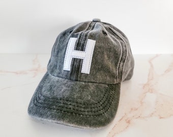May include: A dark grey, distressed baseball cap with a white felt letter 'H' on the front.