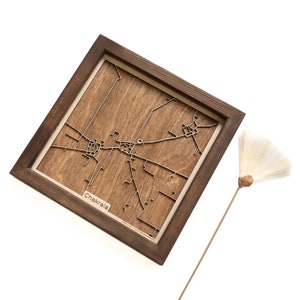 May include: A framed wooden map of the city of Chakala. The map is laser cut and shows the streets of the city. The frame is brown wood.