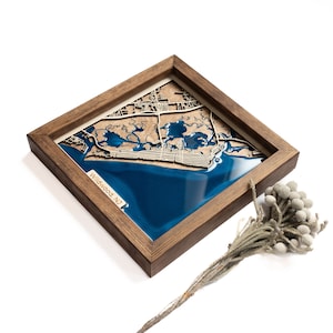 A wooden map of your favourite place enclosed in a wooden frame. It has 3D city streets and epoxy resin water. By adding a pin in a important place for you and an engraving you will make a personalized gift.