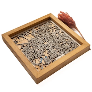 May include: A wooden framed map of Thrissur, India, with a laser-cut design. The map is mounted on a light wood background and framed in a natural wood frame.