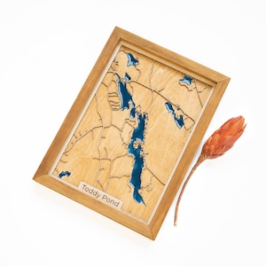 May include: A wooden map of Toddy Pond with blue resin filling the lake. The map is framed in a natural wood frame.