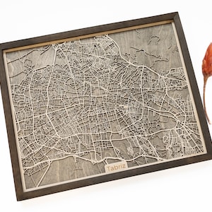 May include: A wooden map of Tabriz, Iran, with a dark brown frame. The map is laser cut and shows the city's streets and landmarks. The map is mounted on a wooden base.