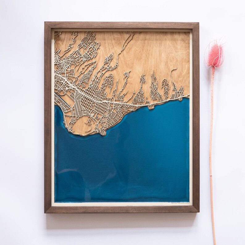 A wooden map of your favourite place enclosed in a wooden frame. It has 3D city streets and epoxy resin water. By adding a pin in a important place for you and an engraving you will make a personalized gift.