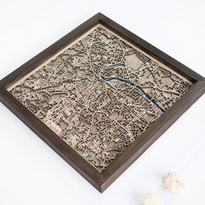 May include: A wooden map of Pune, India, in a dark brown frame. The map is laser cut and shows the city's streets and landmarks. The word "Pune" is visible in the lower left corner of the map.