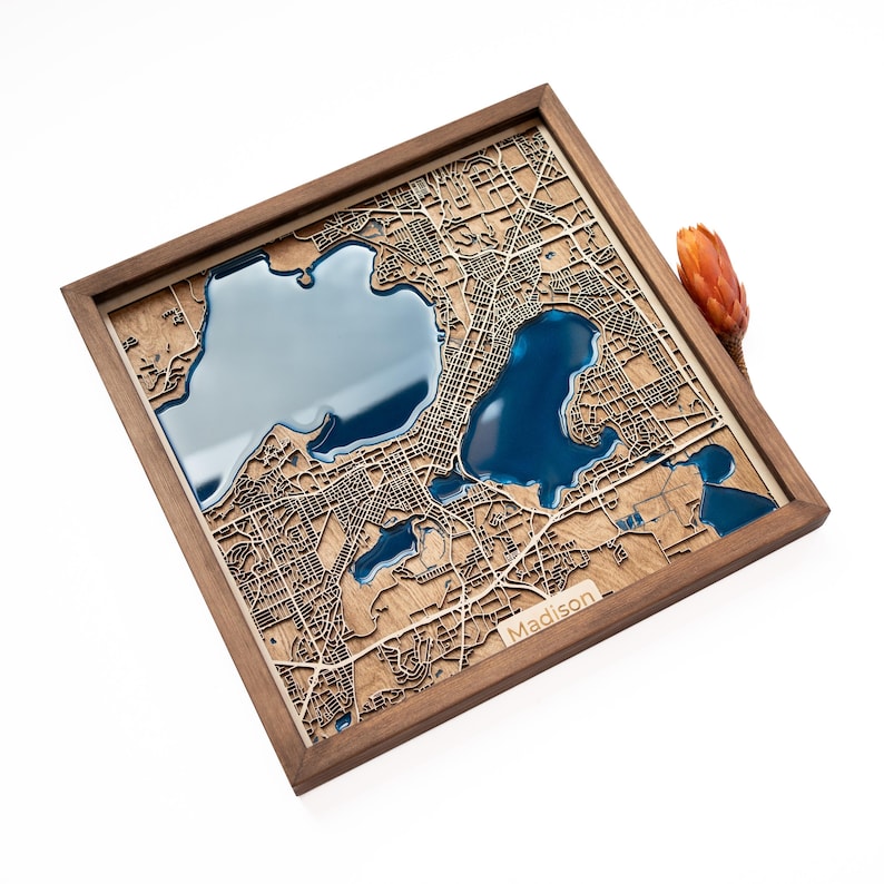 A wooden map of your favourite place enclosed in a wooden frame. It has 3D city streets and epoxy resin water. By adding a pin in a important place for you and an engraving you will make a personalized gift.