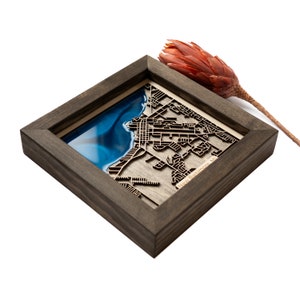 May include: A framed wooden map of New Baltimore, MI with a blue resin inlay representing the water. The map is laser cut and features a detailed street layout.