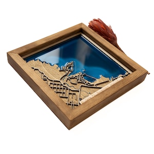 May include: A wooden framed map of Riviere Du Rempart, Mauritius, with a blue resin inlay representing the water. The map is framed in a natural wood frame.
