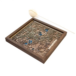 Könnte beinhalten: Eine Holzkarte von Pinneberg, Deutschland, in einem Nussbaumrahmen. Die Karte ist lasergeschnitten und zeigt erhabene Details der Straßen und Wasserwege der Stadt.