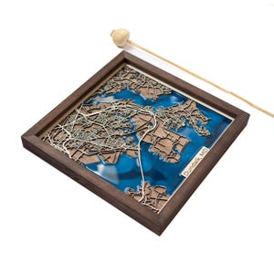 Może przedstawiać: Trójwymiarowa drewniana mapa Dundalk, MD, z niebieską wkładką z żywicy, która reprezentuje wodę. Mapa jest oprawiona w ciemną drewnianą ramę.