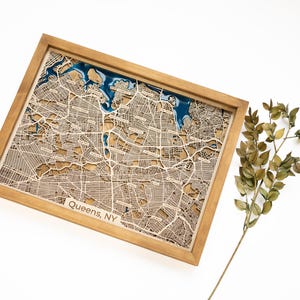 Può includere: Una mappa di legno di Queens, NY, con un riempimento in resina epossidica blu per l'acqua. La mappa è incorniciata in una cornice di legno naturale e ha un effetto 3D in rilievo.