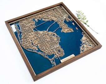 Puede incluir: Un mapa de madera de Tampa Bay, Florida, con una incrustación de resina azul. El mapa está enmarcado en un marco de madera oscura y tiene las palabras "Tampa Bay" inscritas en la esquina inferior derecha.