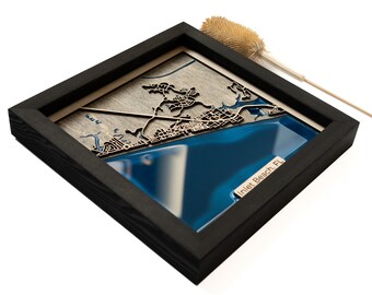 Puede incluir: Un mapa de madera enmarcado de Inlet Beach, Florida, con un océano de resina azul y un contorno de ciudad de madera en relieve. El marco es negro y tiene una textura de madera.