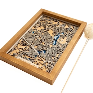 Puede incluir: Un mapa de madera de Arlington, MA, con epoxi azul que llena las características del agua. El mapa está enmarcado en un marco de madera natural.